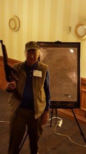 Veteran posing with Thompson SMG in front of map of Iwo Jima